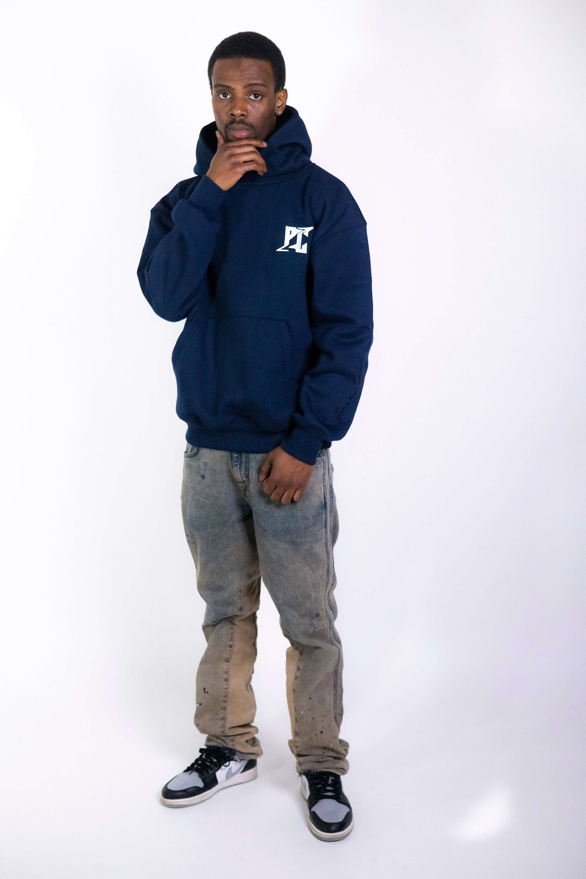 Man wearing navy PC Fusion Script pullover hoody with embroidered logo, paired with distressed jeans and sneakers, showcasing a casual look.